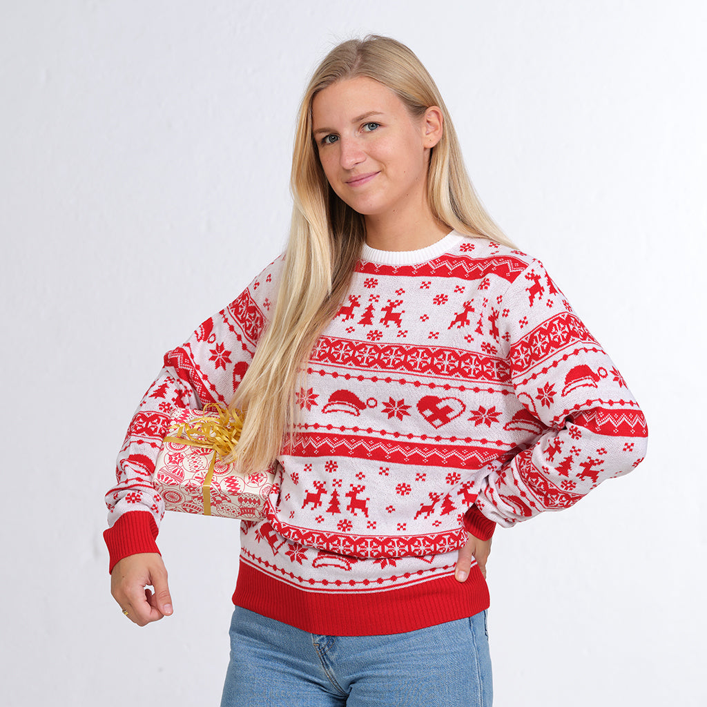 En kvinde poserer med en gave i den ene hånd, mens hun er iført en julesweater.